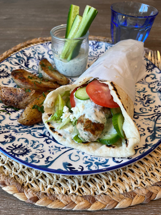Assiette de keftas de poulet à la grecque servies avec tzatziki, feta émiettée, tranches de tomates et rondelles de concombre, accompagnées de pommes de terre rôties à la grecque
